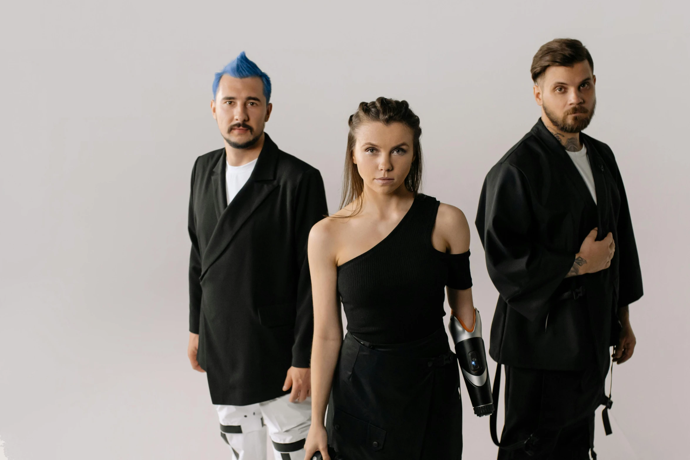 three people standing on a white background, wearing black clothing