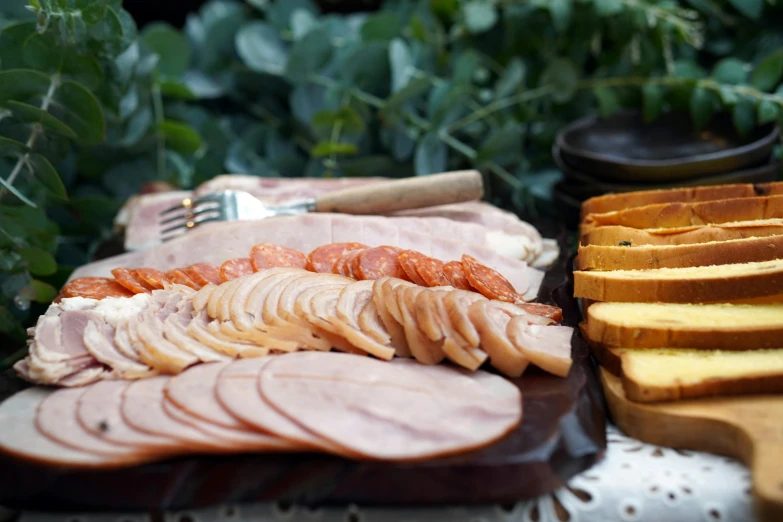 a platter of sliced hams, potatoes and slices of bread on a table