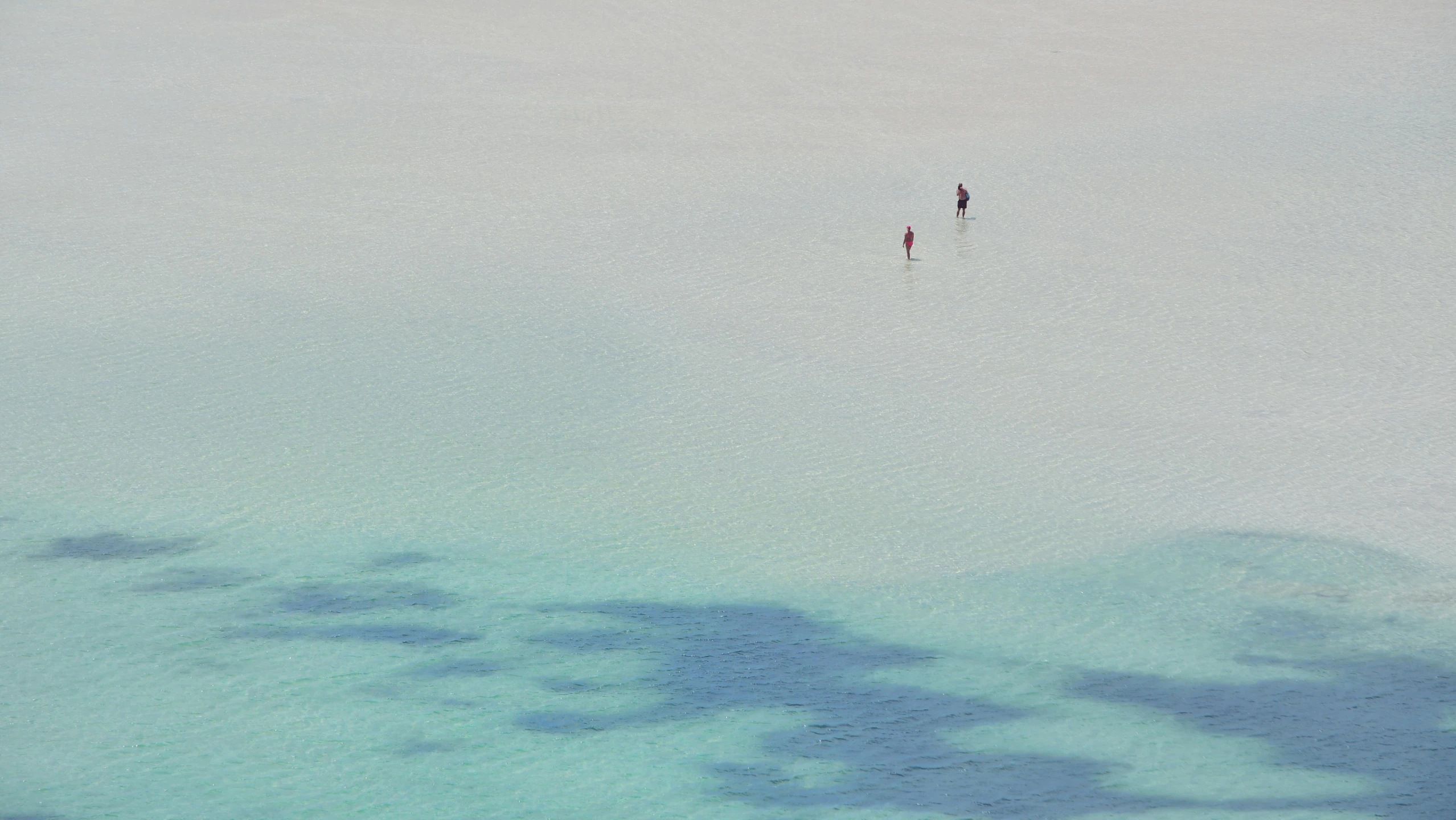 two people walking along an expanse of blue water