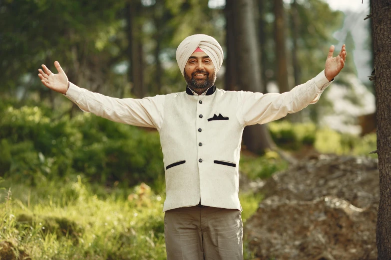 a man in a turban is standing in the woods with his arms outstretched