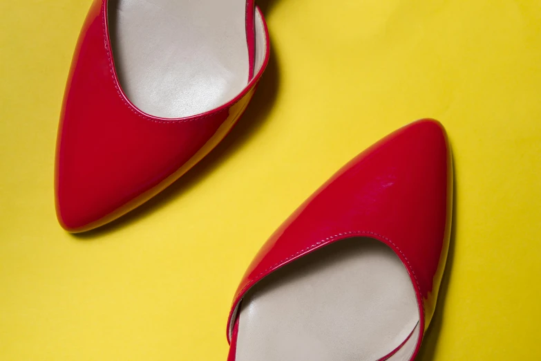 a pair of red women's shoes sits on top of a bright yellow background