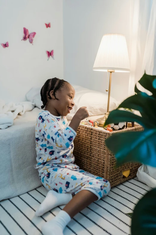 a small girl sitting on a bed next to a basket of toys