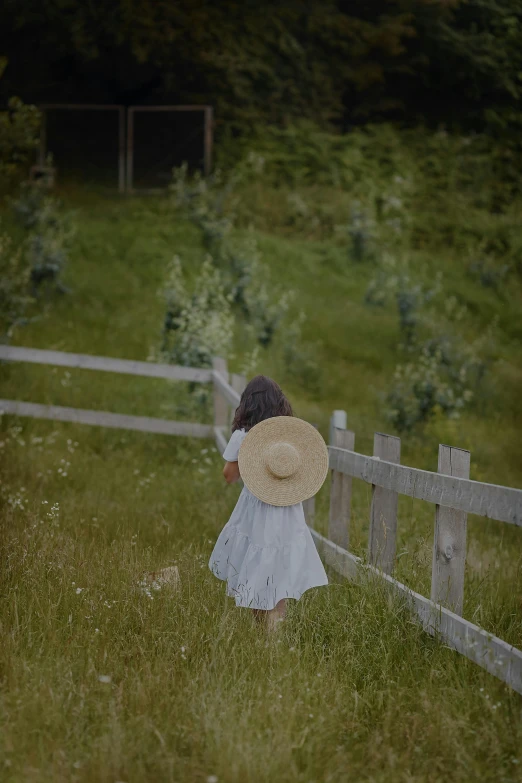 a girl walking in the grass towards a fence