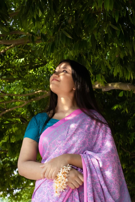 a woman standing under a tree eating soing from her hand