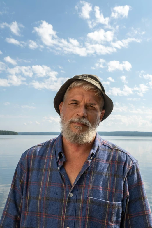 a man wearing a plaid shirt stands in front of water