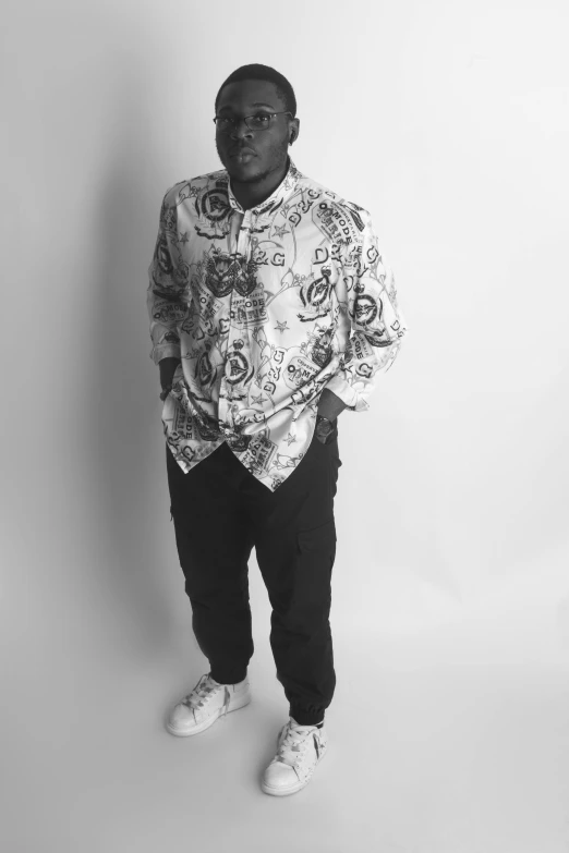 a man standing in front of a white wall wearing an ornate shirt