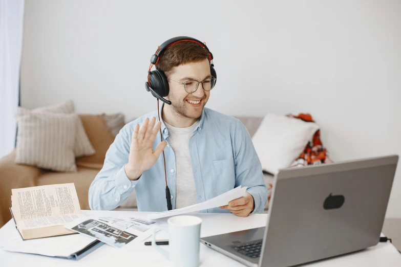 a smiling man with headphones talking on a headset in front of a laptop computer