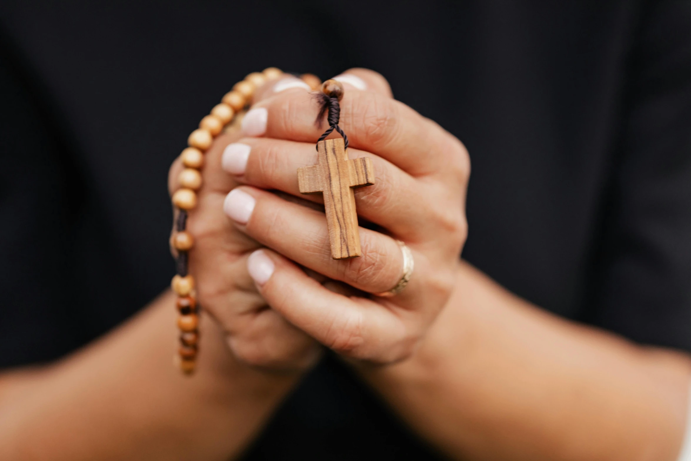 the hand is holding a wooden cross on a chain