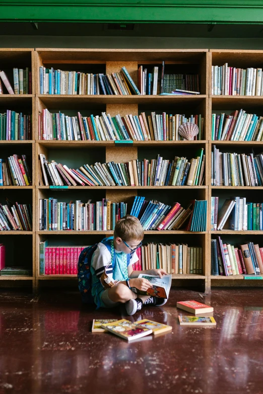 boy sitting on the floor reading in front of bookshelves