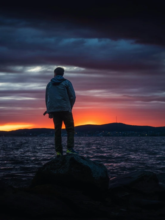 man stands on rock with the sky in front of him