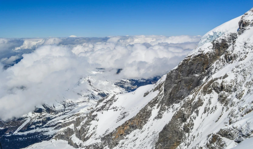 the peaks of snow and some clouds on a sunny day