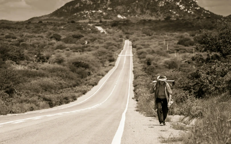 the man walks across a desert road carrying a sack