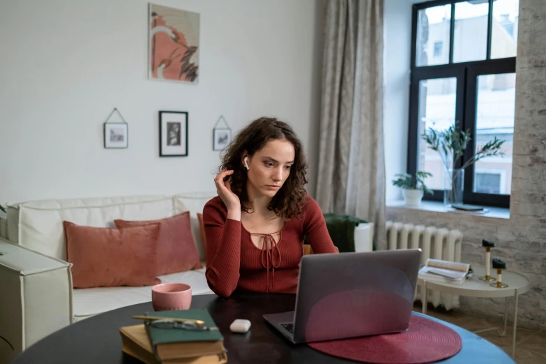 a girl sitting at her home desk with her laptop computer in front of her, as well as a stack of books