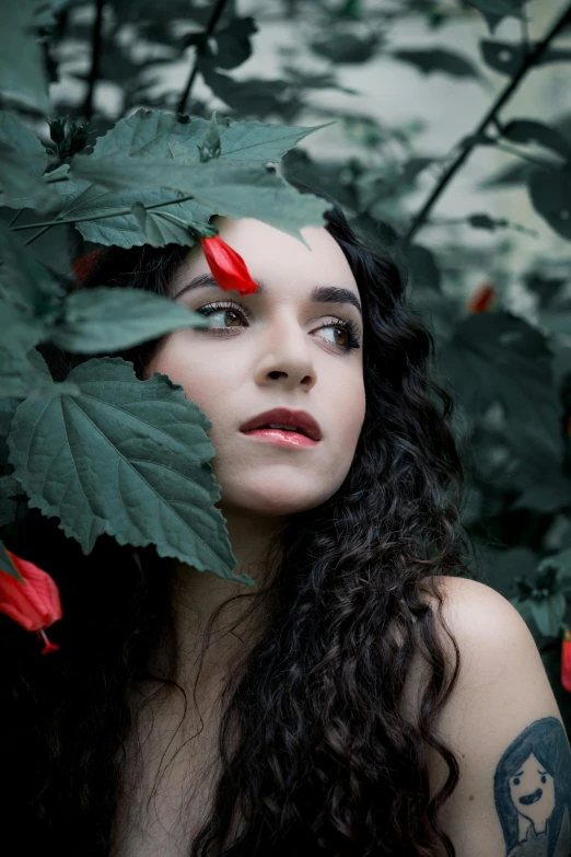 a woman with red flowers on her head behind some leaves