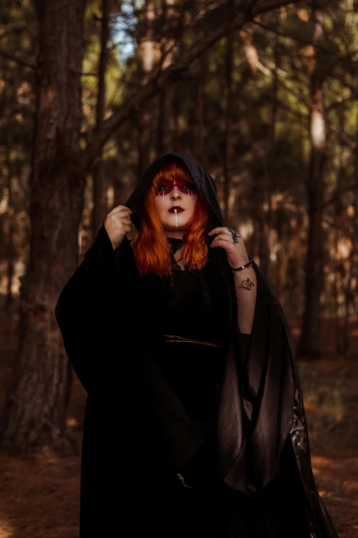 a woman dressed in gothic clothing and makeup poses in the woods