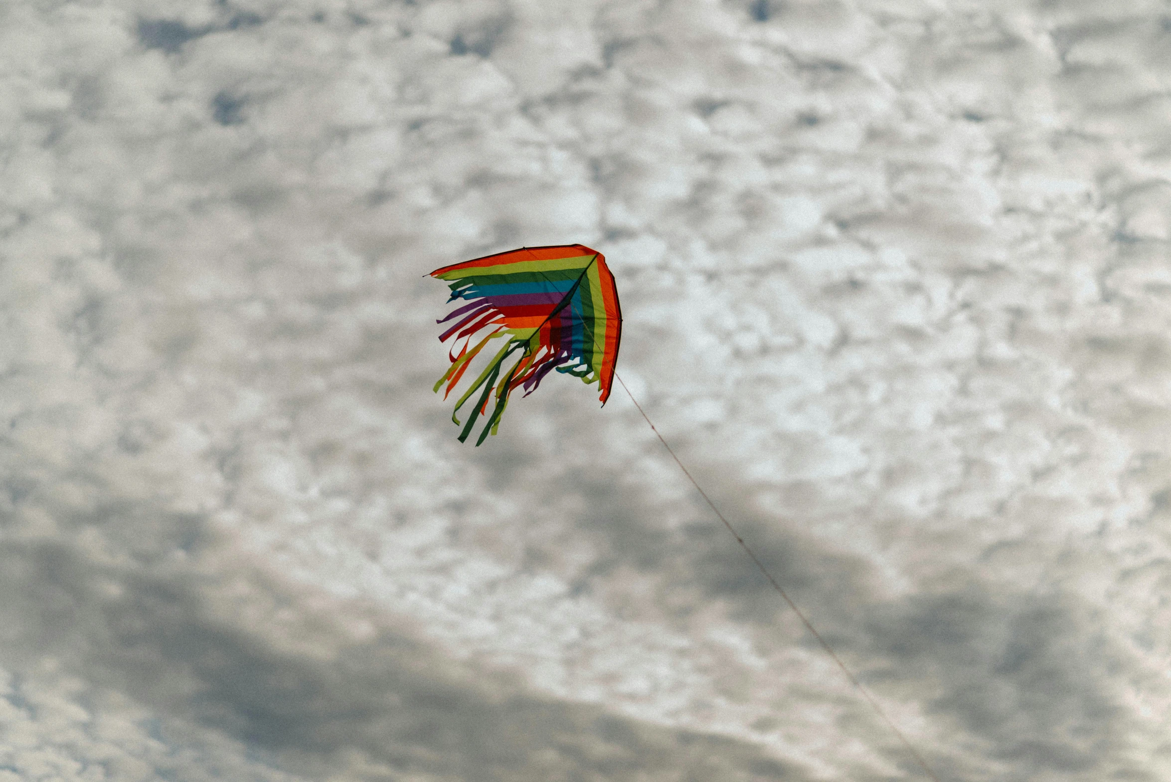 someone flying a rainbow kite in the cloudy sky