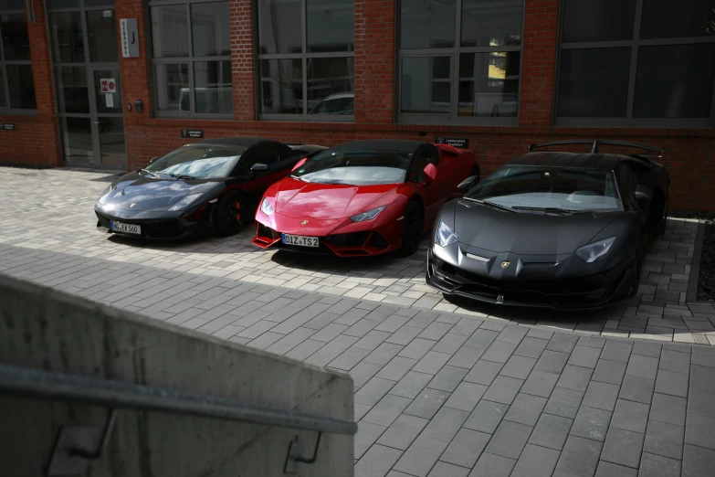 three exotic cars are parked outside of a brick building