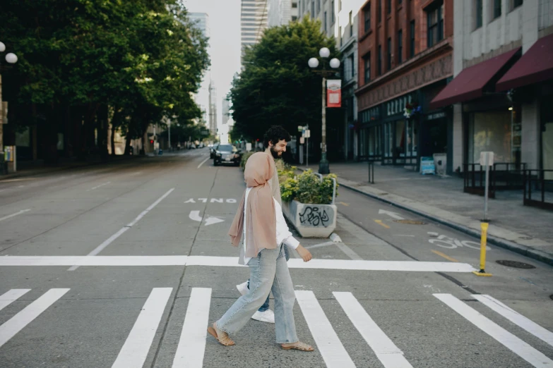 a woman crossing a street with a pink sweater on