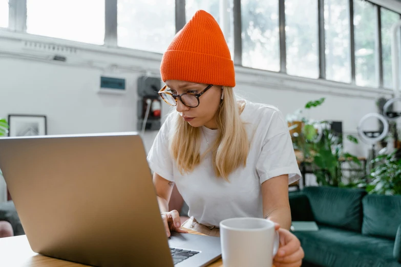 a woman with glasses and an orange hat looks at a laptop