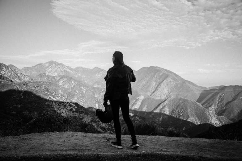 a woman holding a suitcase overlooking a valley and mountains