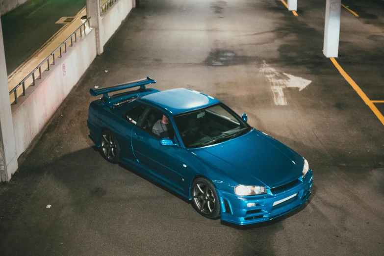 a blue car parked in a parking lot with some trees in the background