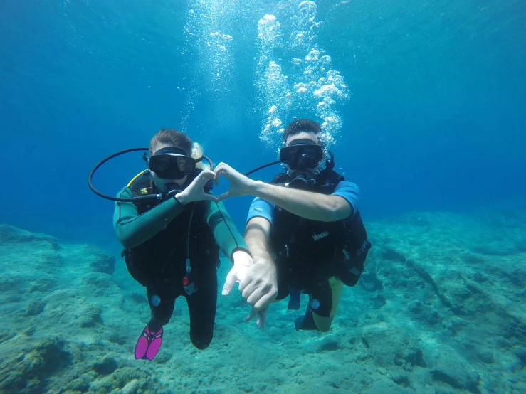 two people in scuba gear point at soing off camera