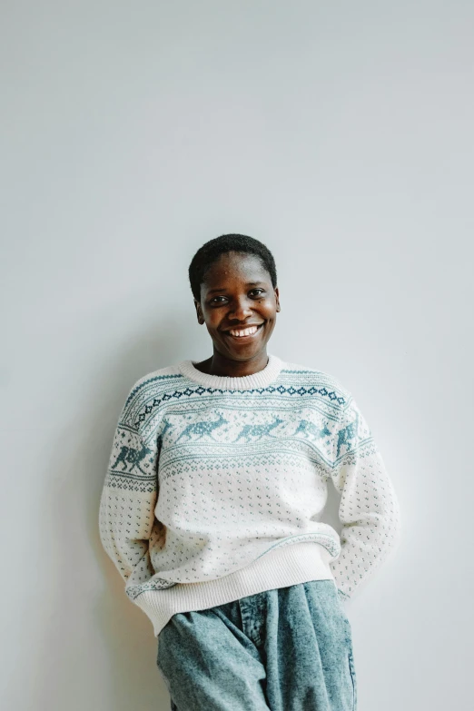 smiling young woman in sweater and pants against a white wall