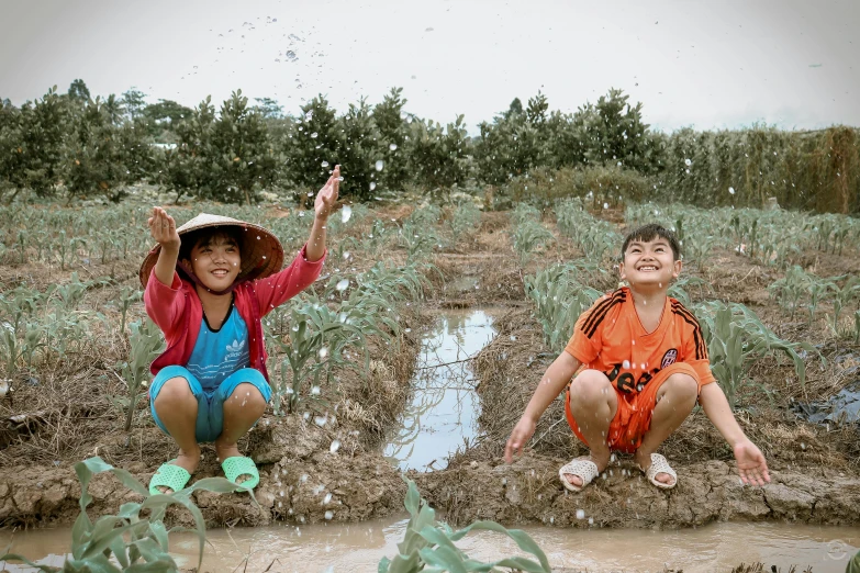 two children kneeling down in muddy, grassy area