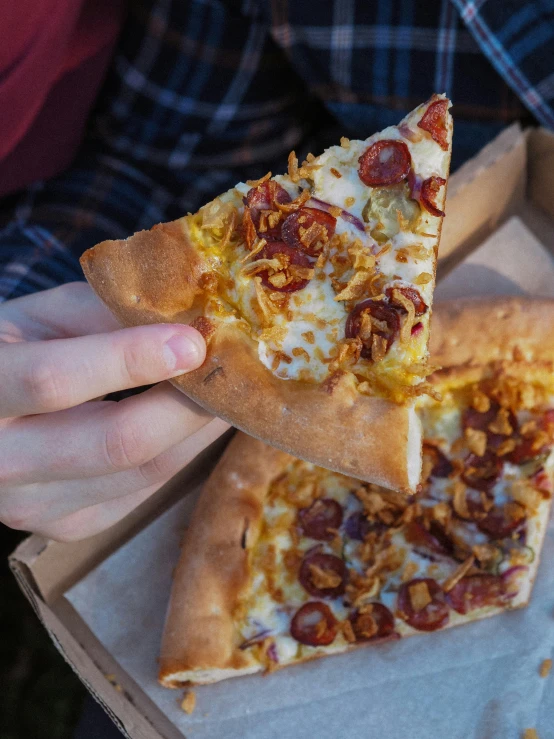 a piece of pizza in a box with someone holding it