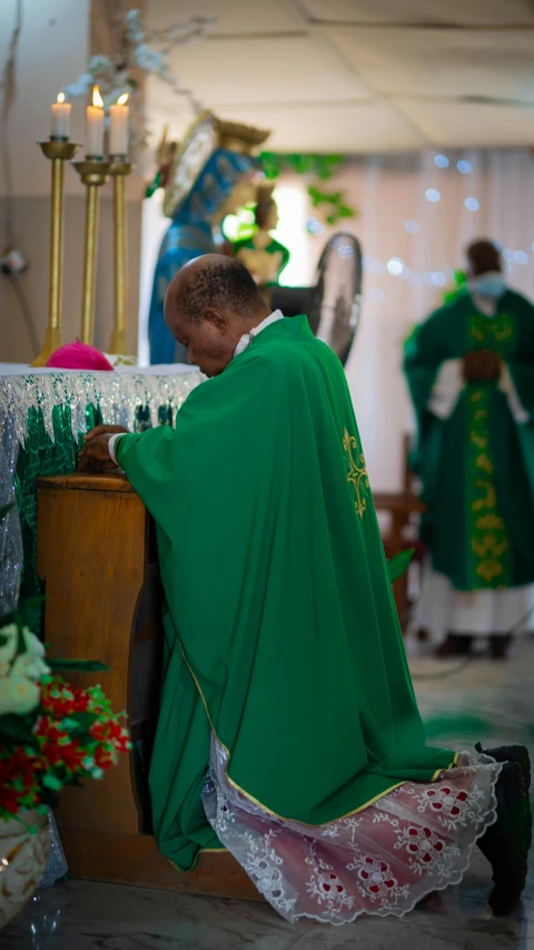 a man with a green cape and lace kneeling down