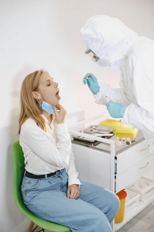 two doctors in white protective clothing, one in blue gloves and the other in light yellow is sitting on a green chair