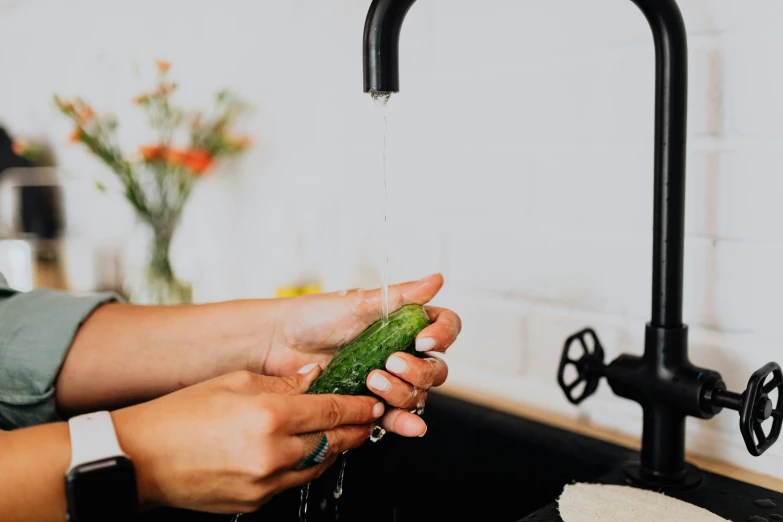 someone holding a cucumber while washing it under the faucet