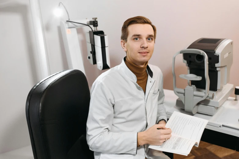 a man in white coat sitting on desk with eye glasses on