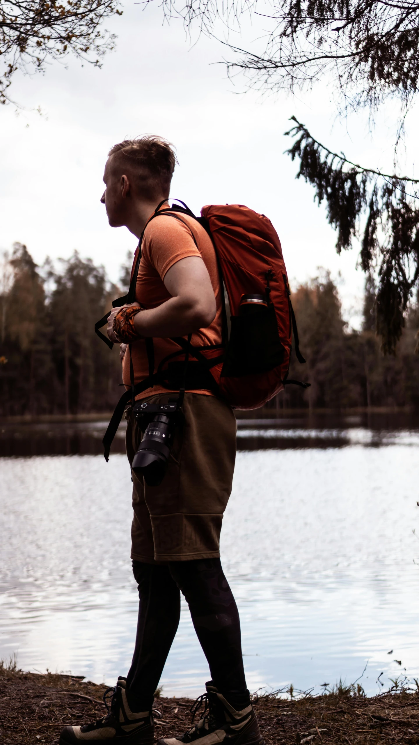 man walking past a small lake with a red backpack