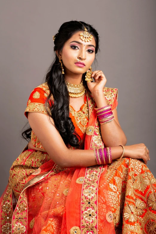 a very pretty indian woman sitting down wearing an orange dress