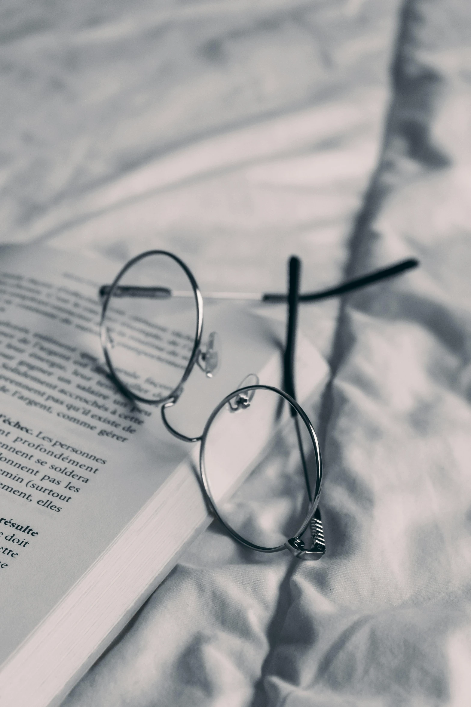 the book on top of the bed is sitting next to the reading glasses