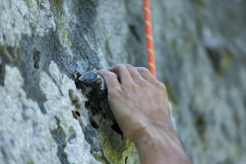 someones hand on the rock climbing up a cliff