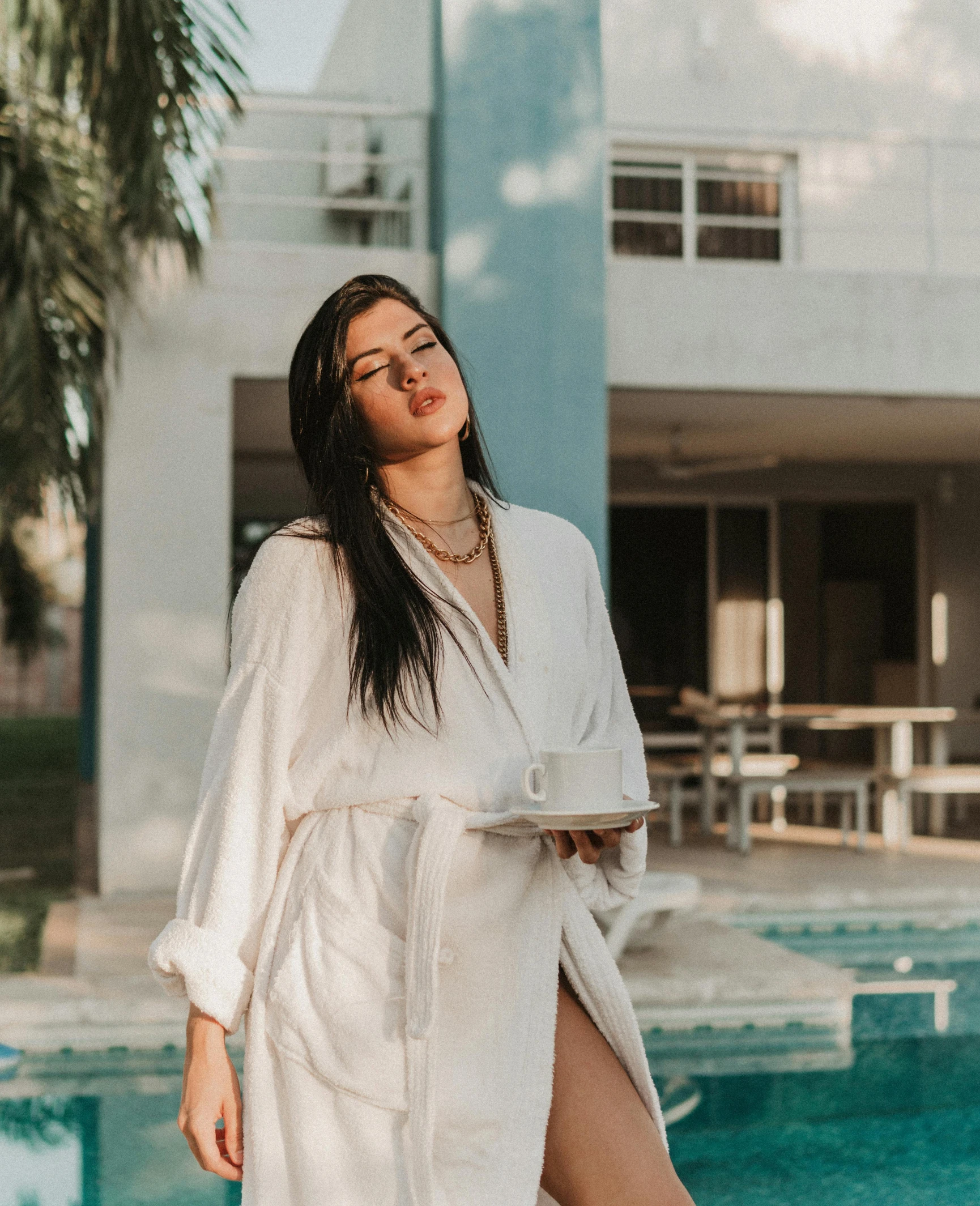 woman in a bathrobe standing by the side of a swimming pool