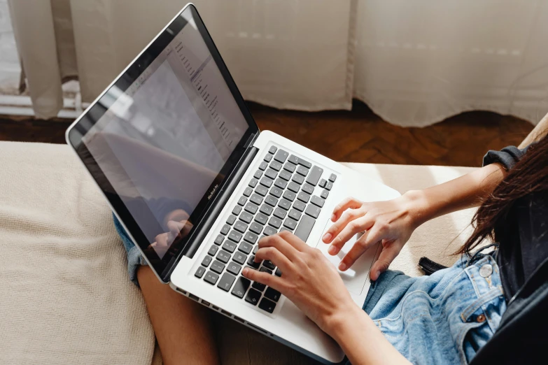 a girl with blue jeans is typing on a white laptop