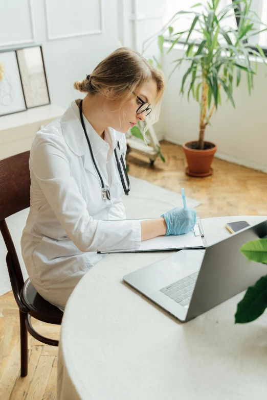 a young woman dressed in scrubs is sitting at a desk while using her laptop computer