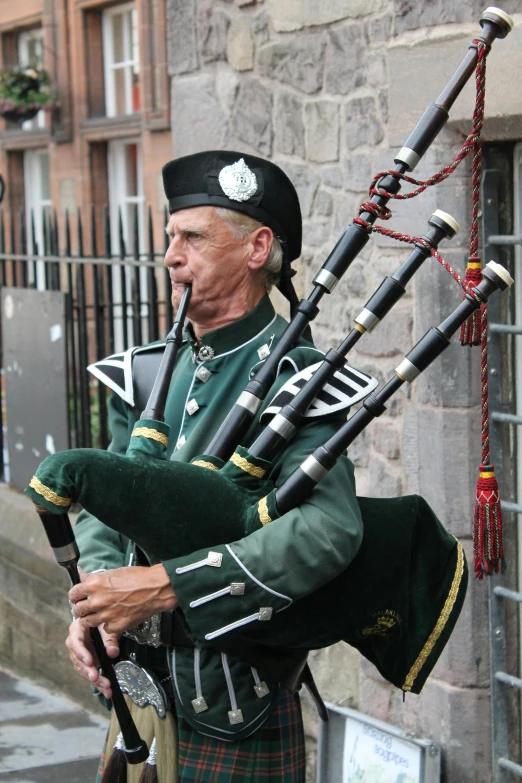 the man is wearing all green while playing his bagpipe