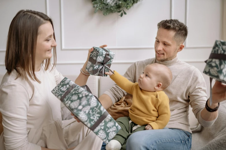 a happy baby is holding a wrapped present while his parents look on