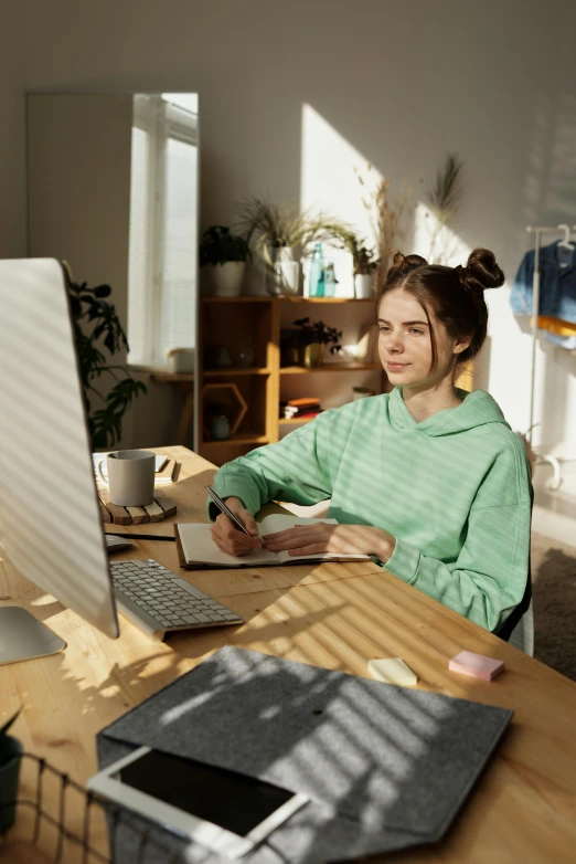 a woman sitting at a desk with an open book, mouse, and computer