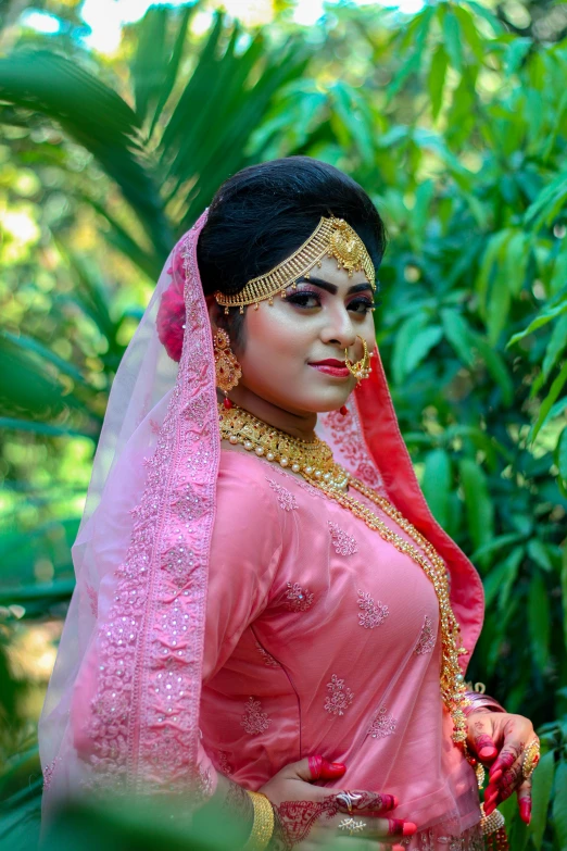 woman in pink outfit posing with her veil covered with red and gold garb