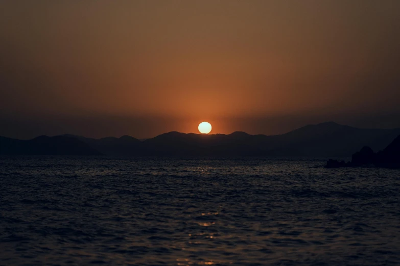 the sun rises above the ocean with small island in the distance