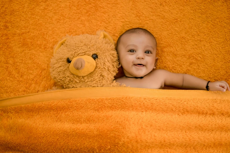 a baby sits between two stuffed animals with orange blanket