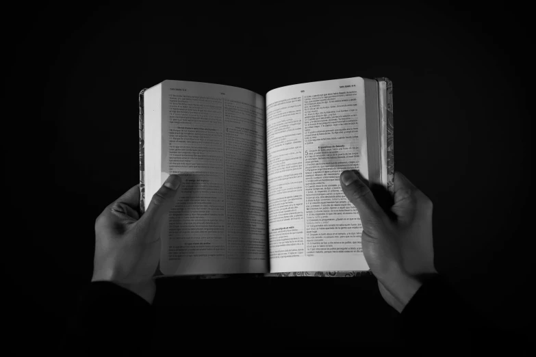 person holding open book in one hand and praying on the other