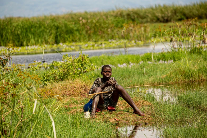 a little boy with a big stick sitting by some water