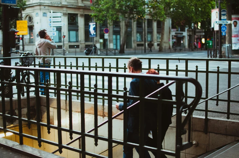 two people looking over a metal railing on a city street