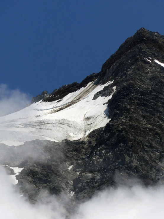 clouds move through the snow covered mountains under a blue sky